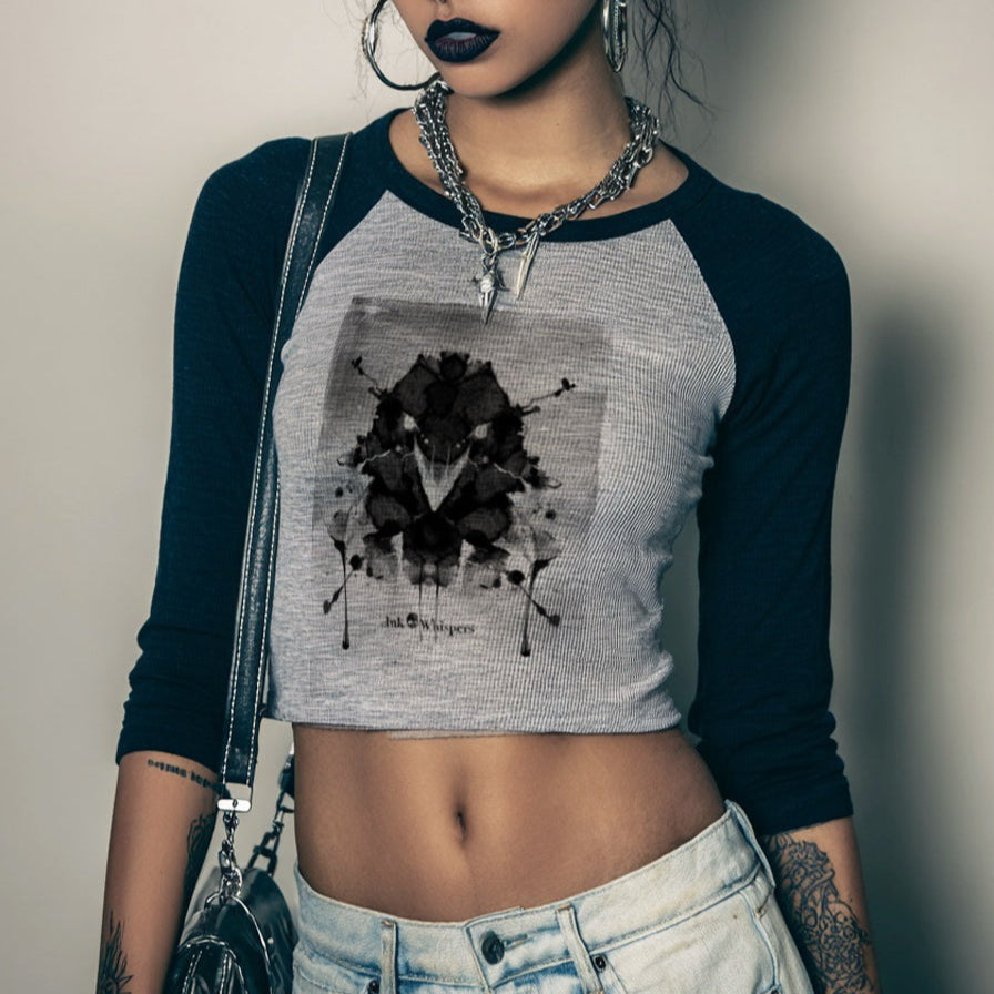 Woman wearing a black and gray long-sleeve crop top with a graphic design, standing against a plain background.