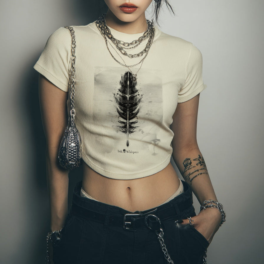 Person wearing a beige t-shirt with a feather design and black pants against a plain background