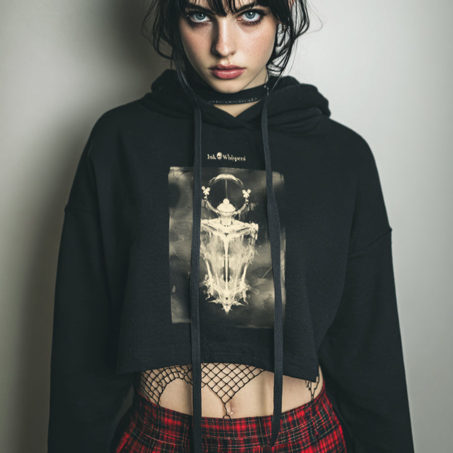Person wearing a black hoodie with a graphic design and a red plaid skirt against a plain background